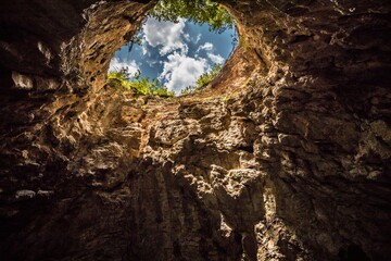 View from below of blue sky with white clouds from the sinkhole in the Caucasus. High rocky walls...