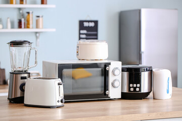 Different household appliances on table in kitchen - obrazy, fototapety, plakaty
