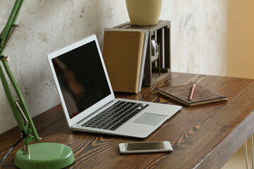 Modern laptop and mobile phone at workplace in room