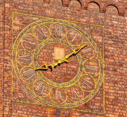 Fototapeta na wymiar A clock with golden coating on a red brick wall in downtown Munich, Germany.