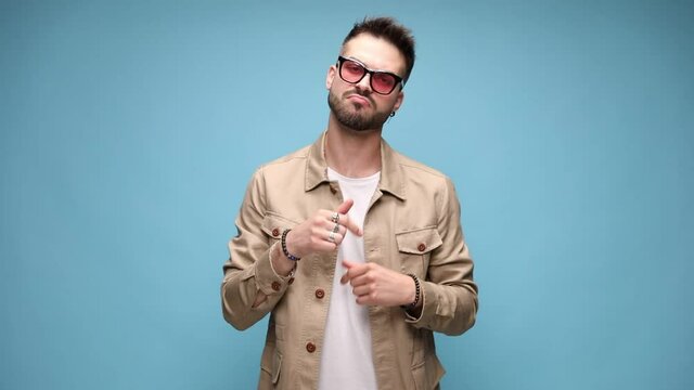 happy young casual man pointing fingers and nominating, dancing and moving, celebrating victory and arranging jacket on blue background
