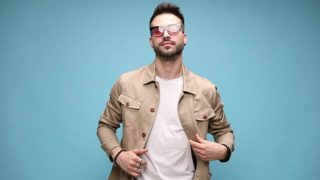 sexy fashion model wearing jacket and glasses, looking to side, running his fingers through hair and fixing it, arranging sleeves and coat, looking down and up, adjusting posture 