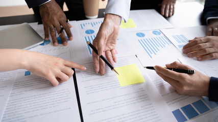 Diverse corporate staff discuss report shown in charts and graphs, analyzing financial stats,...