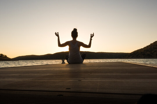 young girl doing yoga poses on a pier at sunset.