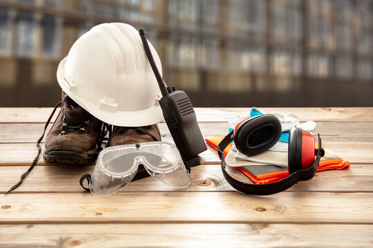 Work safety protection equipment. Industrial protective gear on wooden table, blur construction site background.