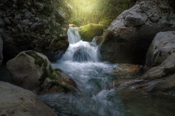 sunlight illuminates a waterfall among huge rocks in the forest