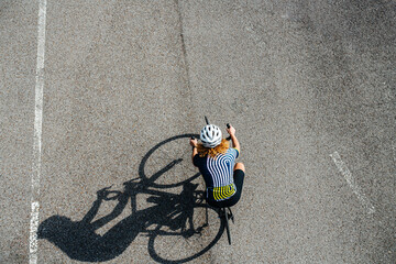 Woman cycling on a professional bike in a white helmet, shot from above © zzzdim