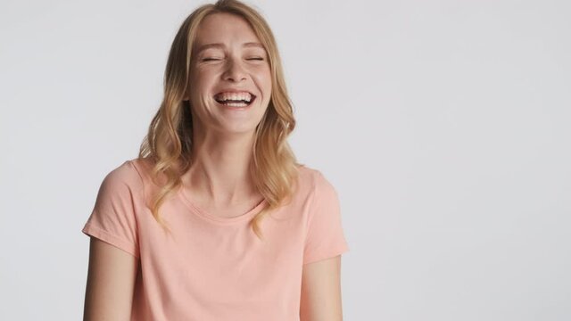 Attractive cheerful blond girl happily laughing on camera over gray background. Happy expression