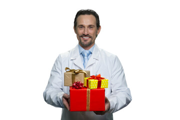Cheerful doctor is holding a pile of presents. Mature medic with gifts isolated on white background.