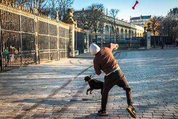 Fototapeta na wymiar Unidentified man is playing with his dog at street throwing a plastic bone. Paris, France.