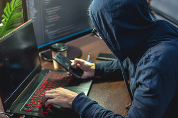 Hacker in the hood is programming virus code at the keyboard for the laptop. Internet fraud and personal data hacking