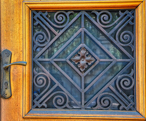 Decorative metal grid as protection for window on wooden entrance door.
