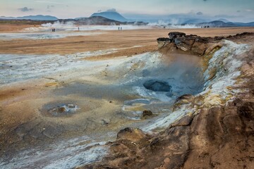 View from above of valley with steaming mud holes and solfataras in the geothermal area in Iceland. Tourists on the background.