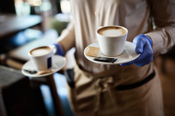 Close-up of waitress wearing protective gloves while serving coffee.