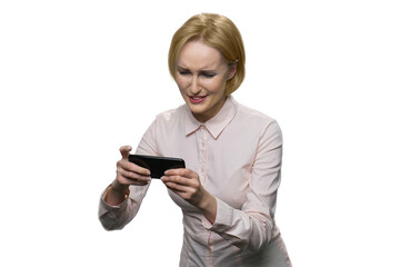 Sad frustrated blond lady's playing video games on her phone. Portrait of mature female office worker entertaining while time break. Isolated on white.