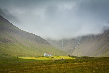 Beautiful green valley between foggy mountains and house lightened with sun. Picturesque landscape. Iceland.