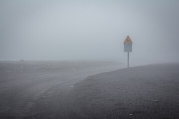 Blue speed limit and yellow windy road signs in foggy Iceland.