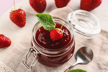 Jar of tasty strawberry jam on table, closeup