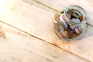 Glass jar with coins, on a wooden background, top view. Finance and investment concept. 