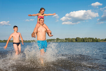 Naklejka premium Father with children jumping together in the water at the beach. Vacation, leisure, way of life. The concept of sport and active play in the summer.