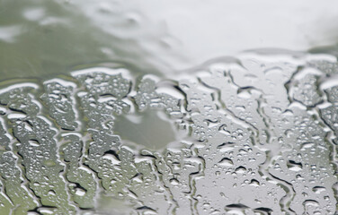 Rain on the windshield of the car causes water beads to adhere to the glass.