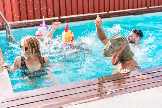 Happy people dancing at pool private party while wearing funny animals masks - Young friends having fun in summer time - Alternative fest during  coronavirus outbreak - Focus on dino face - Powered by Adobe