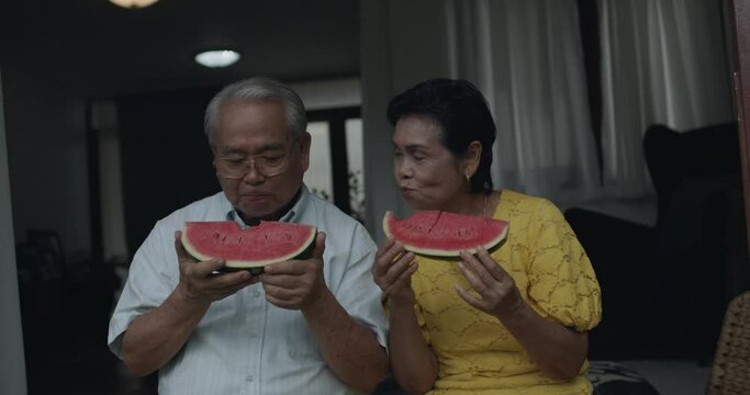 Slow motion and close up of Portrait of happy grandparents, Asian Thai old couple or senior eating watermelon fruit and talking at home