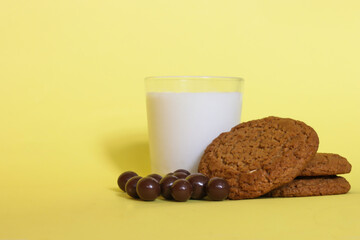 Glass of  milk with oatmeal biscuits and chocolate balls on yellow background