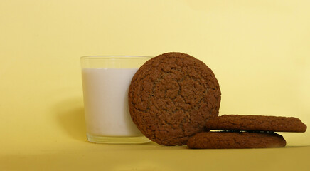 Glass of milk with three round oanmeal biscuits on yellow background