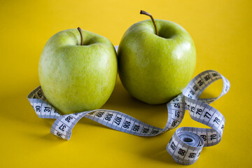 Two green apples on yellow background with tape measure