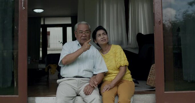 Portrait of happy grandparents, Asian Thai old couple or senior sitting and talking with relax at home and pointing out