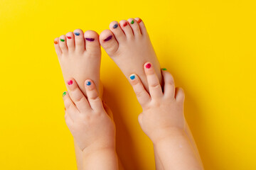Little asian girl with manicure and pedicure on yellow background