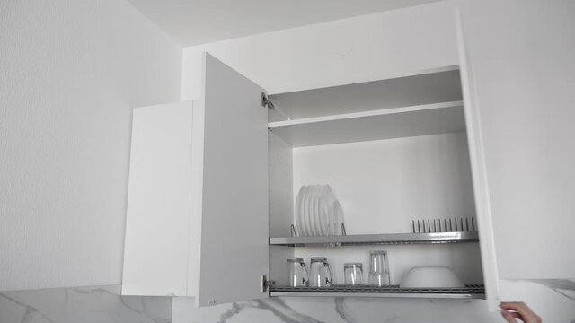 Woman open kitchenware drying rack with plates and cups in white kitchen cabinet