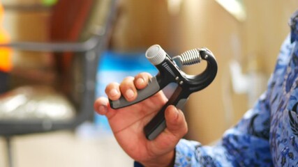 Asian man's arm with hand doing exercise with spring grip, hand ex pander, hand gripper or fitness hand exerciser at home. Clipping path or make selection. Healthy concept - Powered by Adobe