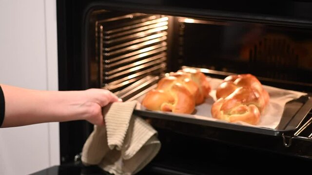 Jewish woman taking out baked Challah Bread out of the oven before Sabbath Jewish Holiday.
