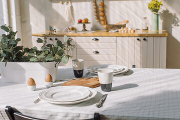 Table served with plates, coffee cups and food for breakfast at modern interior. Family time concept.