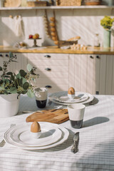 Table served with plates, coffee cups and eggs for breakfast at modern kitchen. Family time, Easter celebration concept.