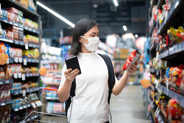 Asian woman wearing hygiene mask prevention virus and pollution ,shopping buying foods at supermarket. New lifestyle with Corona Virus COVID-19.