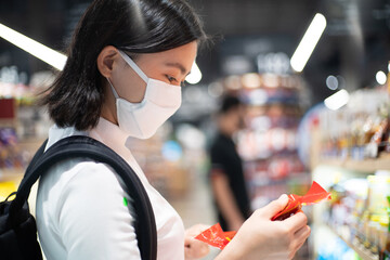 Asian woman wearing protective face mask prevention virus and pollution, shopping buying foods at supermarket. New lifestyle with Corona Virus COVID-19.