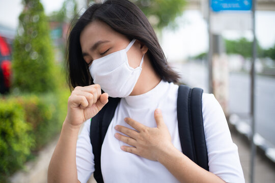 Asian woman wearing protective face mask coughing standing at bus stop. New lifestyle with Corona Virus COVID-19.