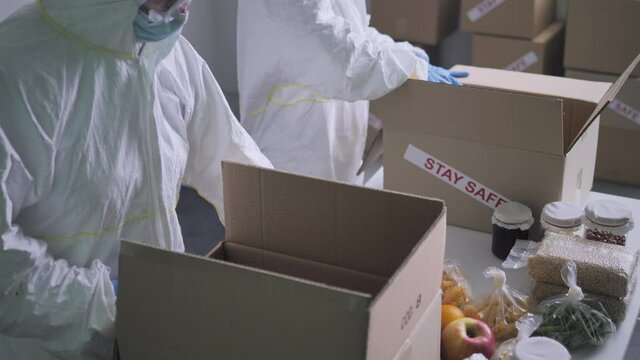 food packaging delivery coronavirus covid-19,charity workers in protective suit pack meals into boxes for needy people,working in a warehouse