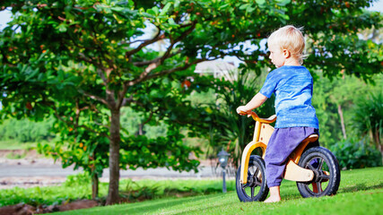 2 - 3 years joyful boy riding a wooden balance bike (run bike). Happy barefoot child learning to wheel, keep balance on training bicycle in the garden. Active kid playing outside. First day on bike.