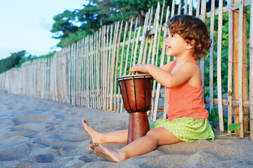 Little happy baby girl play ethnic music on traditional african hand drum djembe, enjoying sunset...