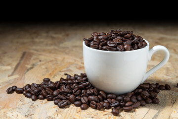 Roasted coffee beans in a white coffee cup on a fragrant wooden table.