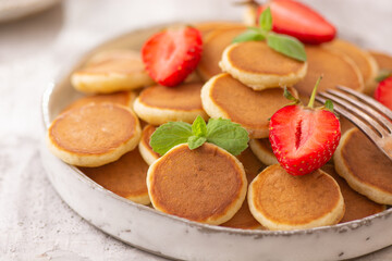 Trendy home breakfast with tiny pancakes and strawberry on white table. 