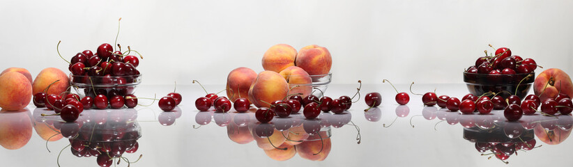 Panorama with peaches and cherries on a glossy table and a light background