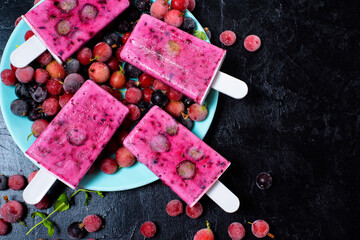 natural organic sorbet four ice cream on a stick with black currant and red berries around . cold milk fruit dessert in summer . top view on a dark background