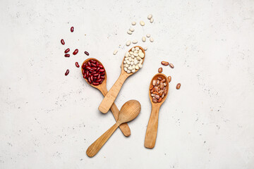 Spoons with raw legumes on light background