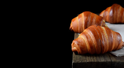Golden croissants of yeast dough on the edge of the wooden table against black background. Copy space