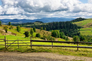 fence on the hill in rural area. early autumn scenery in carpathian mountains. sunny weather with clouds on the sky. hills rolling in tho the distant mountain ridge